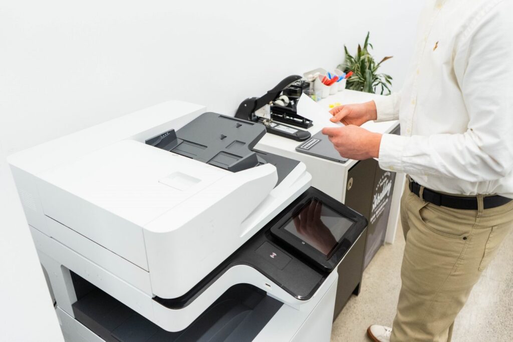 A male employee using white shirt and khaki pants, in front of a printer, picking up his print job