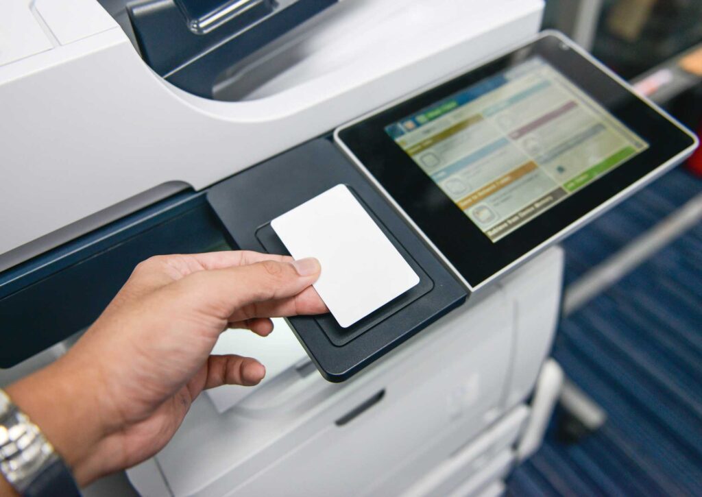A person holding a contactless card above a printer