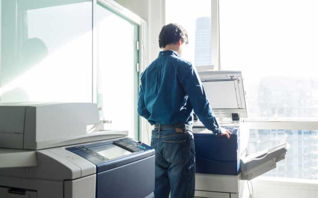 Un hombre en frente a una impresora haciendo una digitalizacion de un documento