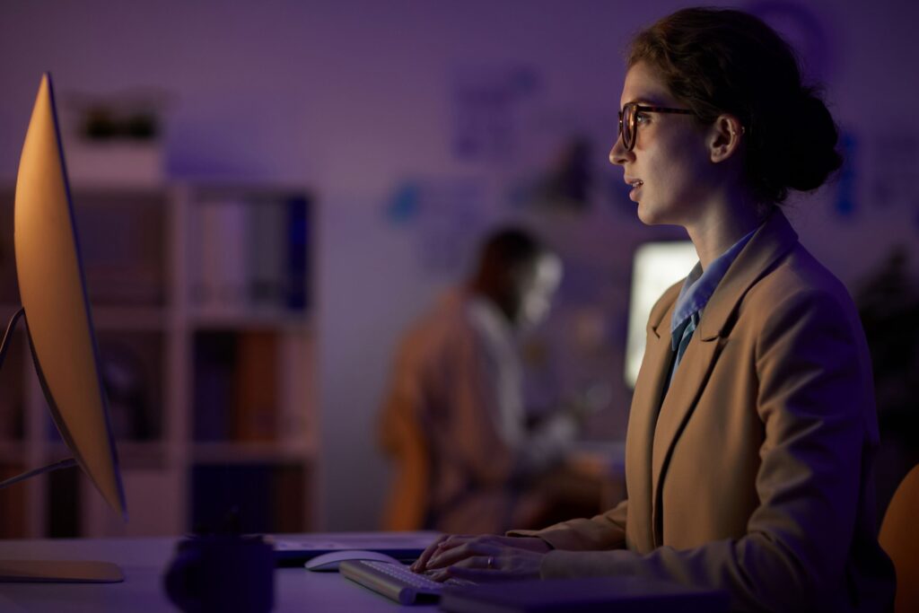 mulher de perfil, sentada em frente ao computador em ambiente escurecido