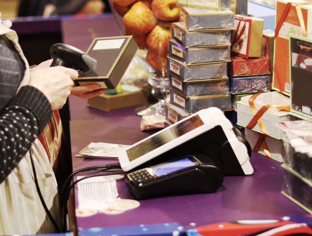 pessoa passando compras com uma máquina de leitura de código de barras e várias caixas ao fundo