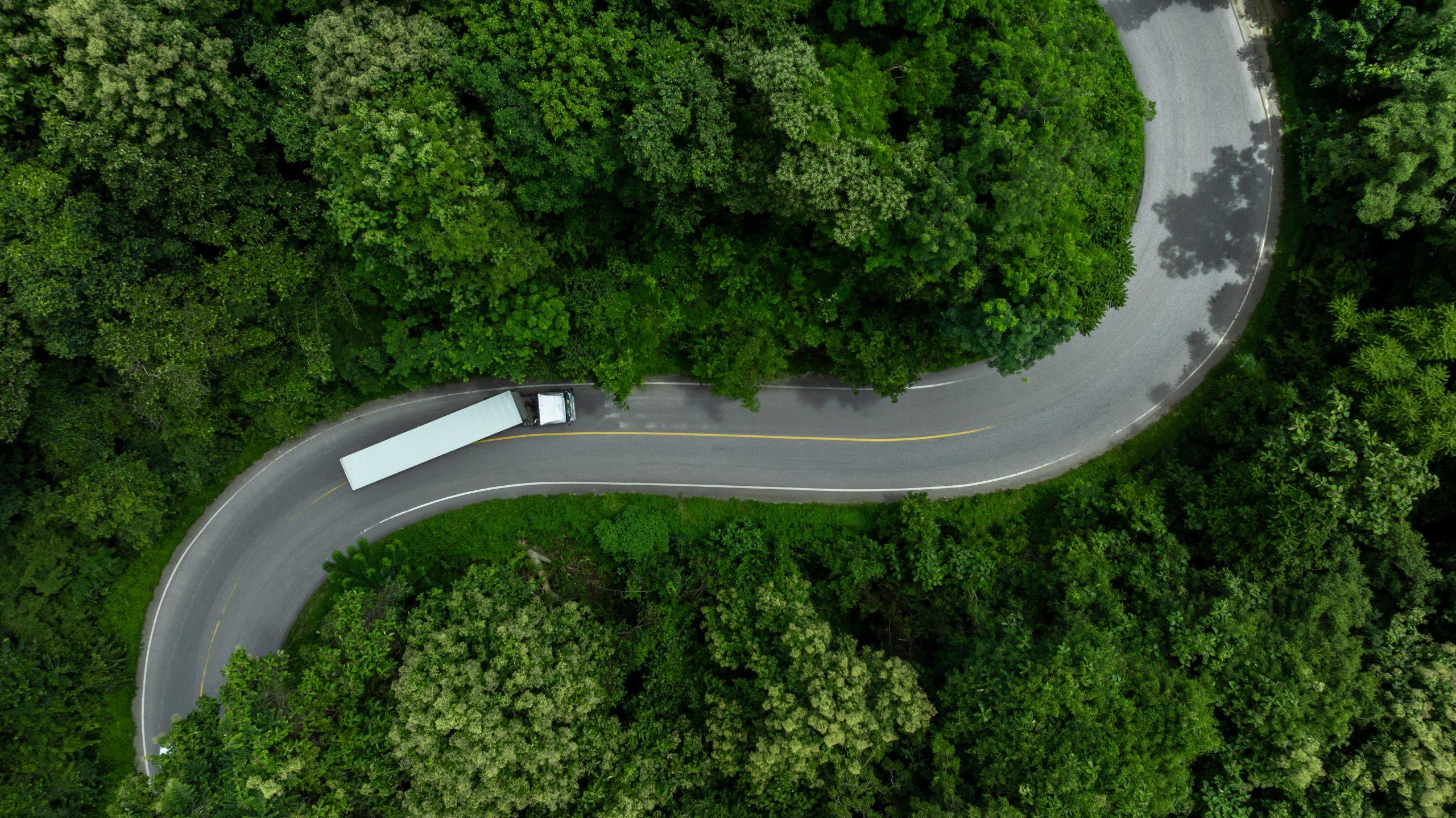 Caminhão em rodovia cercada por vegetação, ilustrando sustentabilidade e ESG no transporte rodoviário de cargas.